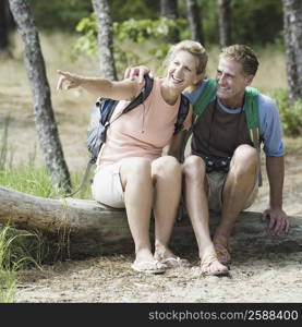 Mature couple sitting on a tree trunk in a forest and pointing