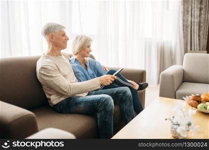 Mature couple sitting on couch and watching TV, happy family. Adult husband and wife resting at home