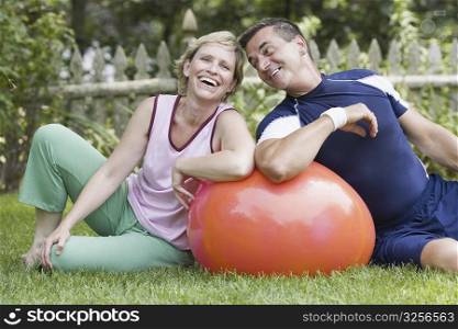 Mature couple sitting on grass with a fitness ball