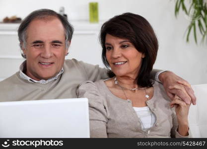 mature couple sitting on sofa with laptop