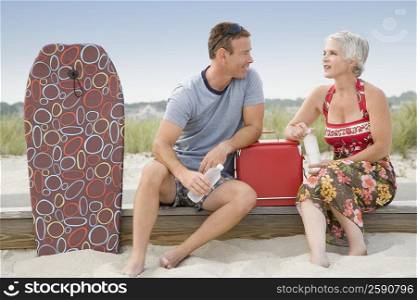 Mature couple sitting on the beach and drinking water