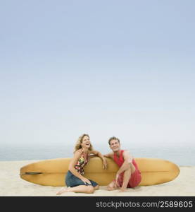 Mature couple sitting on the beach with a surfboard