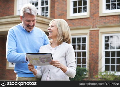 Mature Couple Standing Outside House Looking At Property Details