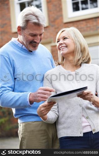Mature Couple Standing Outside House Looking At Property Details