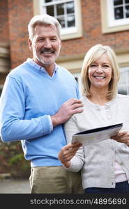 Mature Couple Standing Outside House Looking At Property Details