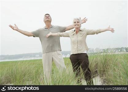Mature couple standing with their arm outstretched in a grassy field
