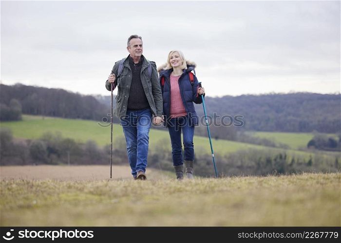 Mature Couple Walk Through Fall Or Winter Countryside Using Hiking Poles