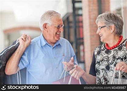 Mature couple walking along street, carrying shopping bags, laughing