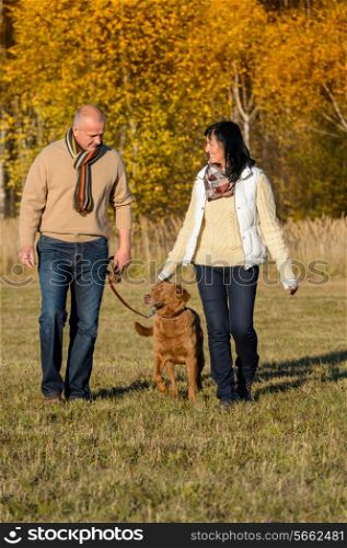 Mature couple walking retriever dog enjoying autumn sunny park