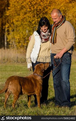 Mature couple with retriever dog embracing in autumn sunny park
