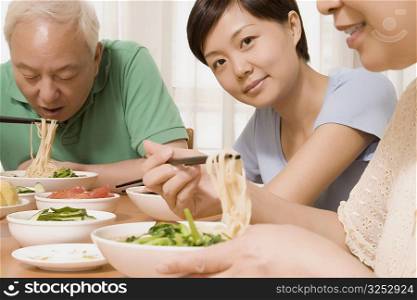 Mature couple with their daughter sitting at a dining table and having noodles