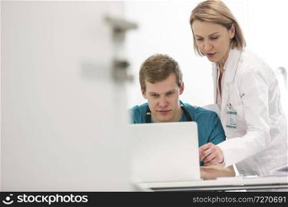 Mature doctor discussing with young nurse over laptop at desk in hospital