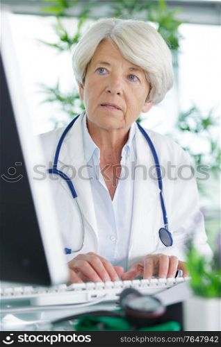 mature doctor sitting at computer and communicates with patient friendly