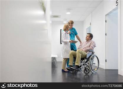 Mature doctor with digital tablet explaining patient on wheelchair at hospital