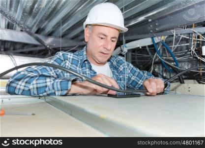 mature electrician fixing wiring in the ceiling