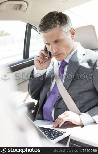 Mature executive using laptop while talking on mobile phone in car