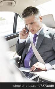 Mature executive using laptop while talking on mobile phone in car
