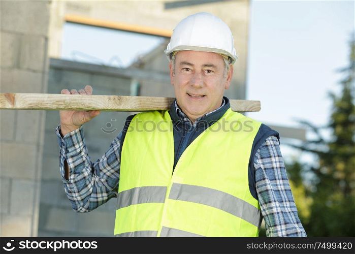 mature factory worker carrying long wooden board