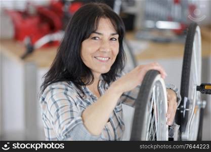 mature female bicycle mechanic repairing wheel in a workshop