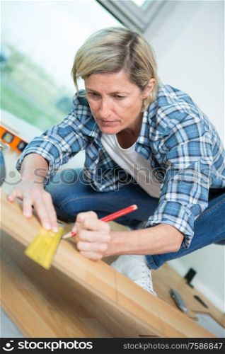 mature female carpenter marking on wood with pencil in workshop