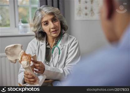 Mature Female Doctor Meeting With Male Patient Discussing Joint Pain In Hip Using Anatomical Model