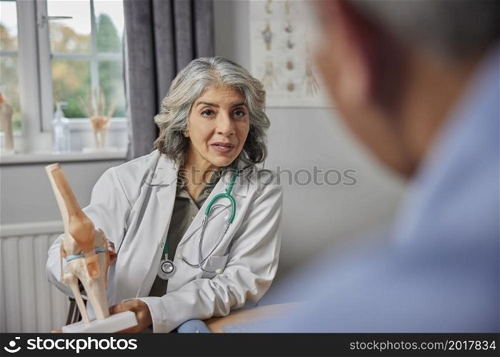 Mature Female Doctor Meeting With Male Patient Discussing Joint Pain In Knee Using Anatomical Model