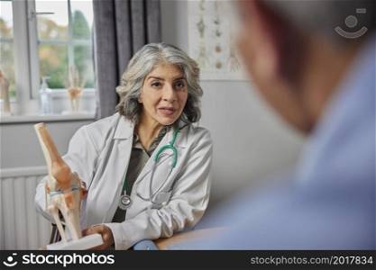 Mature Female Doctor Meeting With Male Patient Discussing Joint Pain In Knee Using Anatomical Model