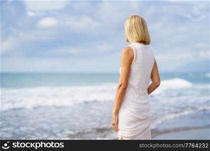 Mature female gazing serenely at the sea. Elderly woman enjoying her retirement at a seaside location.. Mature female gazing serenely at the sea. Elderly woman standing at a seaside location
