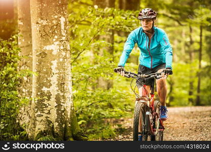 Mature female mountain biker cycling on forest trail