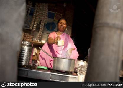Mature female tea vendor preparing chai on gas stove at market stall
