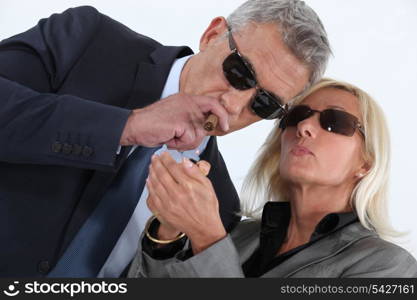 mature gentleman smoking cigar with blonde spouse showing off