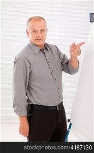 Mature handsome businessman pointing at empty flip chart looking front