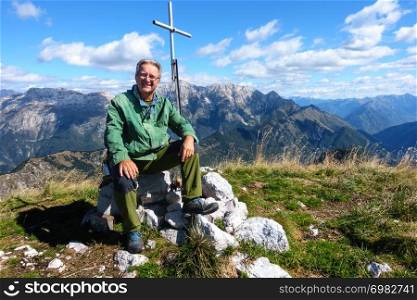 Mature hiker sitting on peak and smiling and looking on camera.
