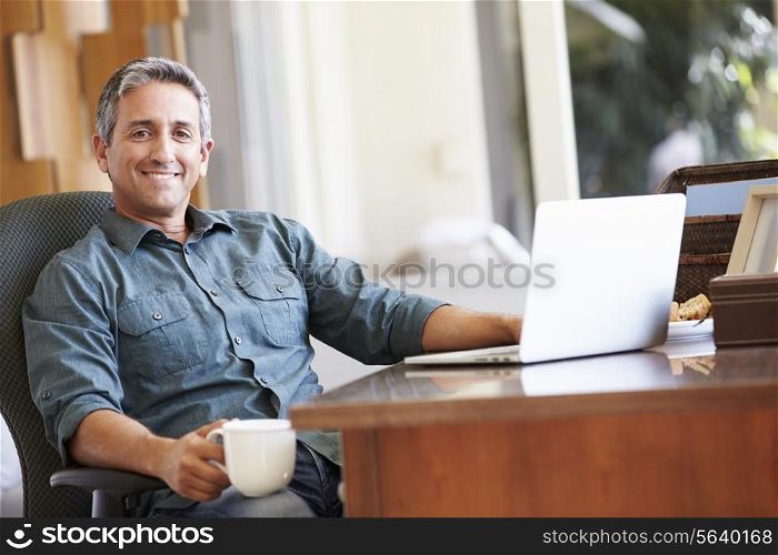 Mature Hispanic Man Using Laptop On Desk At Home