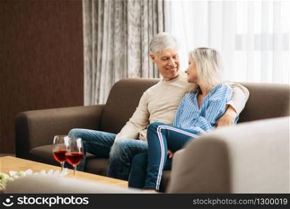 Mature husband and wife sitting on couch and hugs, happy family. Adult love couple resting at home. Mature husband and wife sitting on couch and hugs