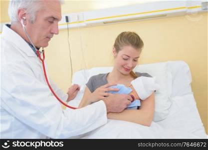 mature male doctor examining baby girl with mother watching
