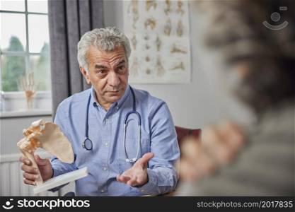 Mature Male Doctor Meeting With Female Patient Discussing Joint Pain In Shoulder Using Anatomical Model