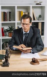 mature male lawyer reading book with gavel justice statue wooden table