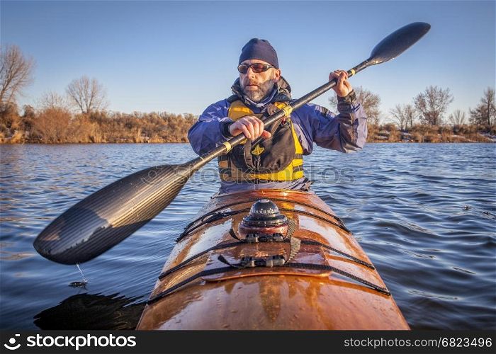 mature male paddler exercising with a wing carbon fiber paddle in a home built wooden sea kayak on lake, fall scenery in Colorado, view from kayak bow