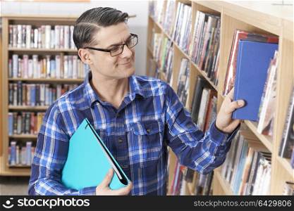 Mature Male Student Taking Book From Shelf In Library