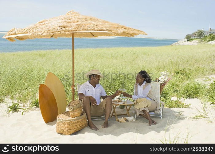 Mature man and a mid adult woman toasting with wine glasses on the beach