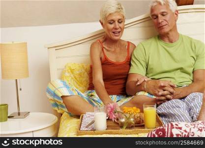 Mature man and a senior woman sitting on the bed and having breakfast