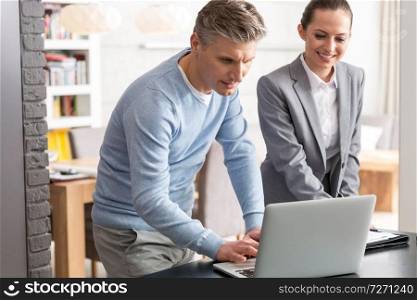 Mature man and saleswoman discussing over laptop table in apartment