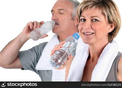 Mature man and woman in sportswear drinking water