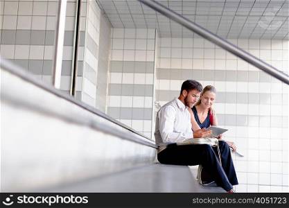Mature man and woman sitting on steps, looking at digital tablet