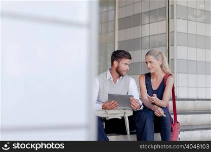 Mature man and woman sitting outdoors, looking at digital tablet