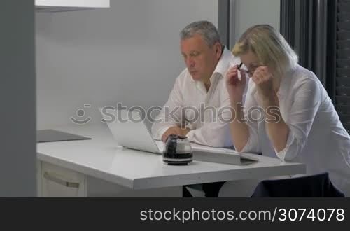 Mature man and woman with laptop and tablet PC working on business indoor. They drinking coffee when doing job