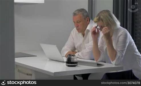 Mature man and woman with laptop and tablet PC working on business indoor. They drinking coffee when doing job