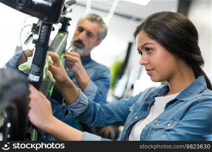 mature man and young woman working on bicycle in workshop