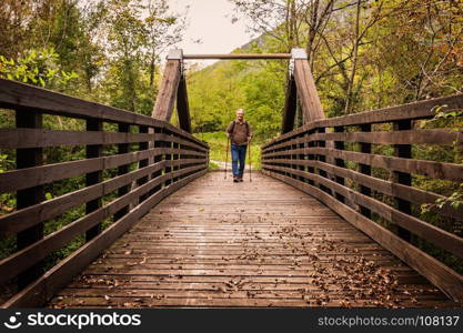 Mature man are hiking in the mountains, walking on a wooden bridge